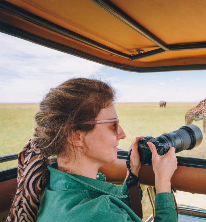 A tourist observing a group of elephants in the wild Masai Mara, Kenya, during a sunset. Group safari packages