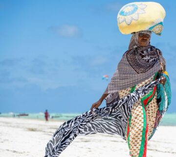 African woman in Zanzibar wearing a colorful traditional dress, walking through a historic Stone Town