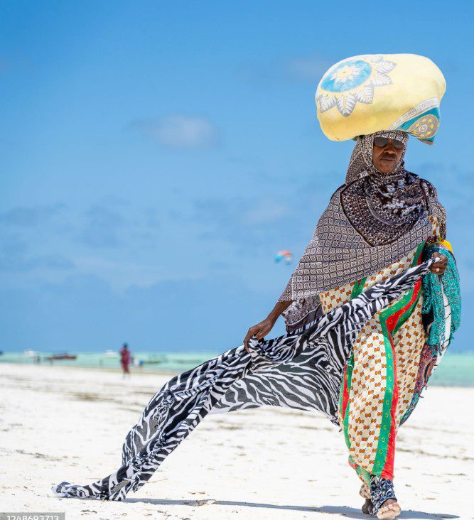 African woman in Zanzibar wearing a colorful traditional dress, walking through a historic Stone Town