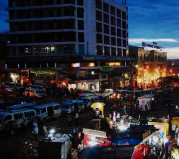 Busy street scene in Kampala at night with lights, people, and motorcycles 