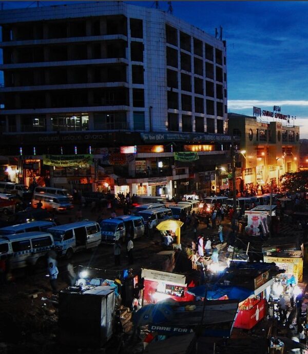 Busy street scene in Kampala at night with lights, people, and motorcycles.