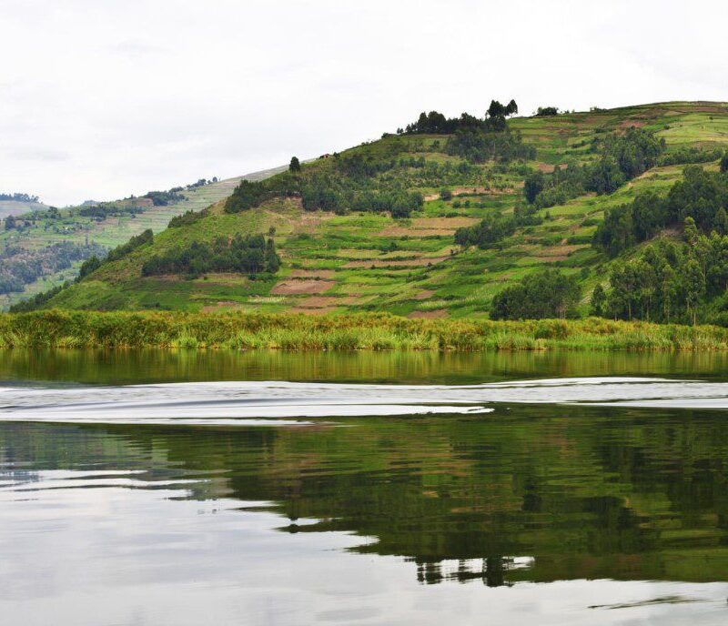 Scenic view of Lake Bunyonyi surrounded by lush green hills and traditional Ugandan village homes.