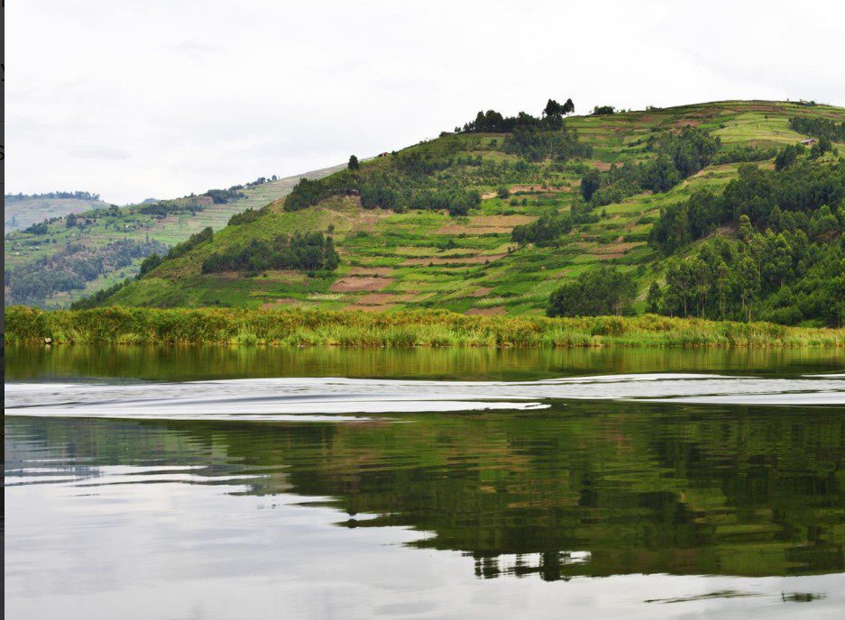 Scenic view of Lake Bunyonyi surrounded by lush green hills and traditional Ugandan village homes.