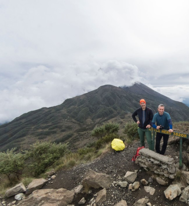 Hikers ascending Mount Meru with scenic mountain views in the background during a high-altitude trekking adventure.