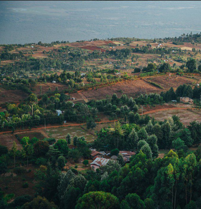 A paraglider soaring above Kenya's scenic Rift Valley with lush hills and expansive landscapes below.