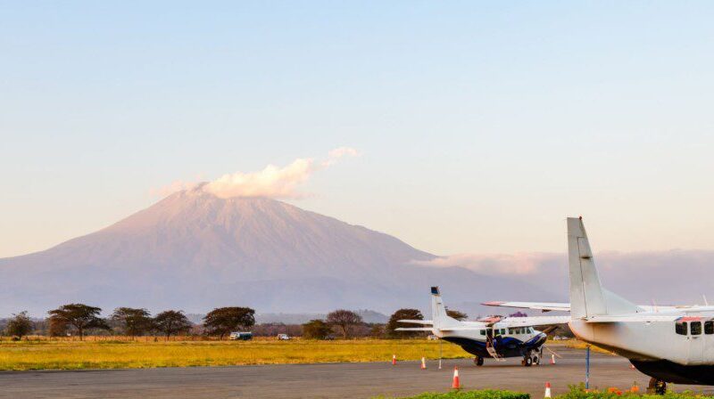 Small safari aircraft parked at a remote Serengeti airstrip with wildlife and savannah landscape in the background.