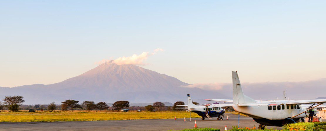 Small safari aircraft parked at a remote Serengeti airstrip with wildlife and savannah landscape in the background.