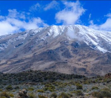 Mount Kilimanjaro towering above the African landscape, with its snow capped summit and diverse ecosystems 
