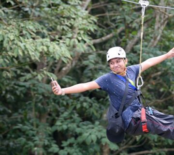 Person zip lining through a lush green forest canopy in East Africa, surrounded by trees and scenic natural landscapes 
