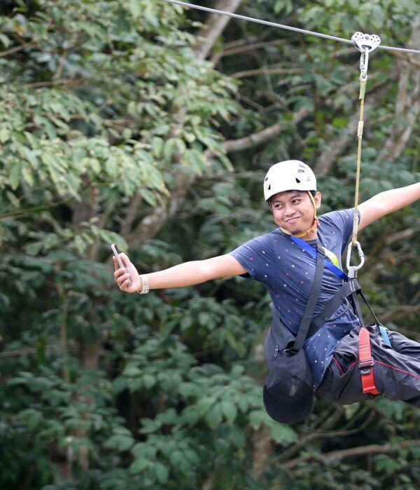 Person zip-lining through a lush green forest canopy in East Africa, surrounded by trees and scenic natural landscapes.