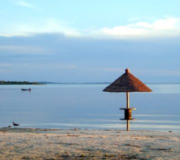 Thatched beach umbrella on the calm shore of a Ssese Island with a distant fishing boat