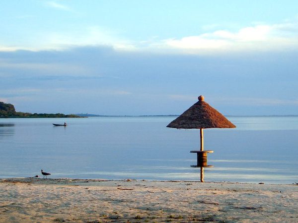 Thatched beach umbrella on the calm shore of a Ssese Island with a distant fishing boat